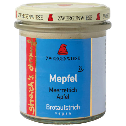 Glas mit Brotaufstrich Mepfel, einer cremigen Mischung aus Äpfeln und Honig, auf einem Holztisch mit frischen Äpfeln und einem Messer daneben.