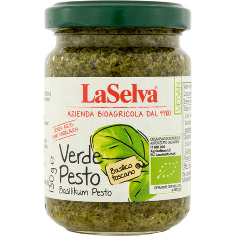 Glas mit grünem Pesto, gefüllt mit frischen Basilikumblättern, Pinienkernen, Knoblauch und Parmesan, auf einem rustikalen Holztisch arrangiert.