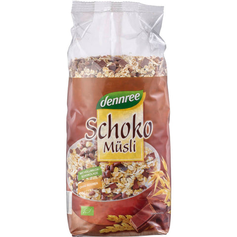 Eine Schüssel mit knusprigem Schoko Müsli, gefüllt mit Haferflocken, Schokoladenstückchen und Nüssen, auf einem Holztisch mit einem Löffel daneben.